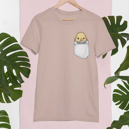 Beiges, lässiges T-Shirt mit einem charmanten Küken, das aus einer Brusttasche lugt, kombiniert mit der Botschaft Tierschutz